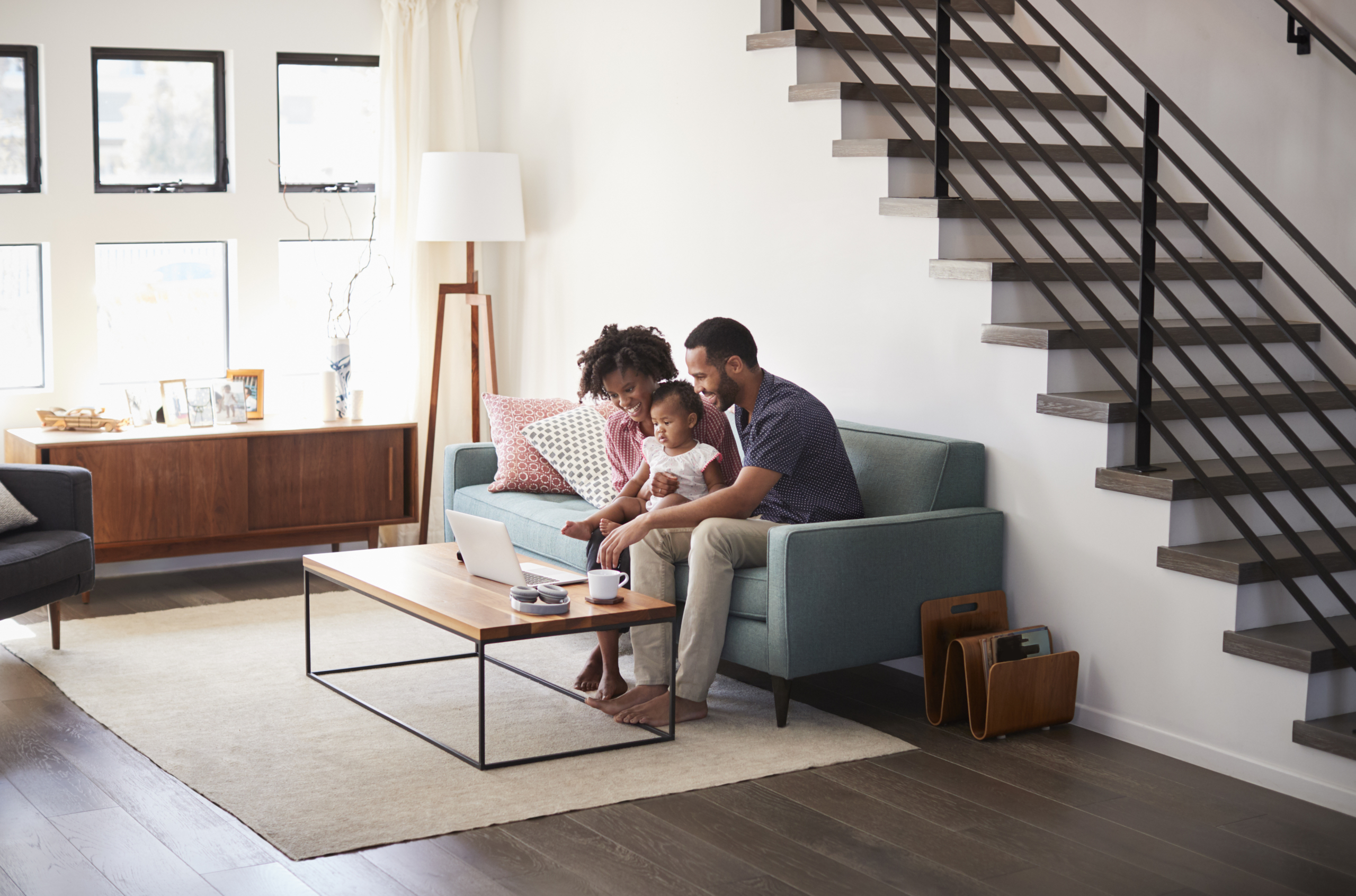 Family With Baby Daughter Sitting On Sofa At Home Looking At Laptop Computer